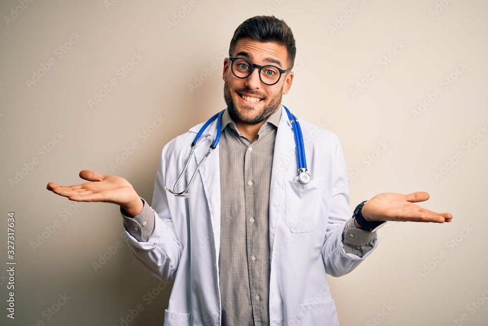 Young doctor man wearing glasses, medical white robe and stethoscope over isolated background clueless and confused expression with arms and hands raised. Doubt concept. Young doctor man wearing glasses, medical white robe and stethoscope over isolated background clueless and confused expression with arms and hands raised. Doubt concept.