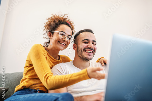 Young attractive happy couple sitting at home and surfing on internet over laptop. Woman is hugging her beloved boyfriend.