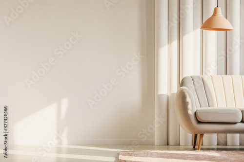 Copy space on empty white wall of fashionable living room with pastel orange lamp and white sofa in the corner