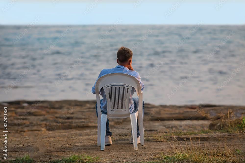 Fototapeta premium young man sits in a plastic chair by the sea