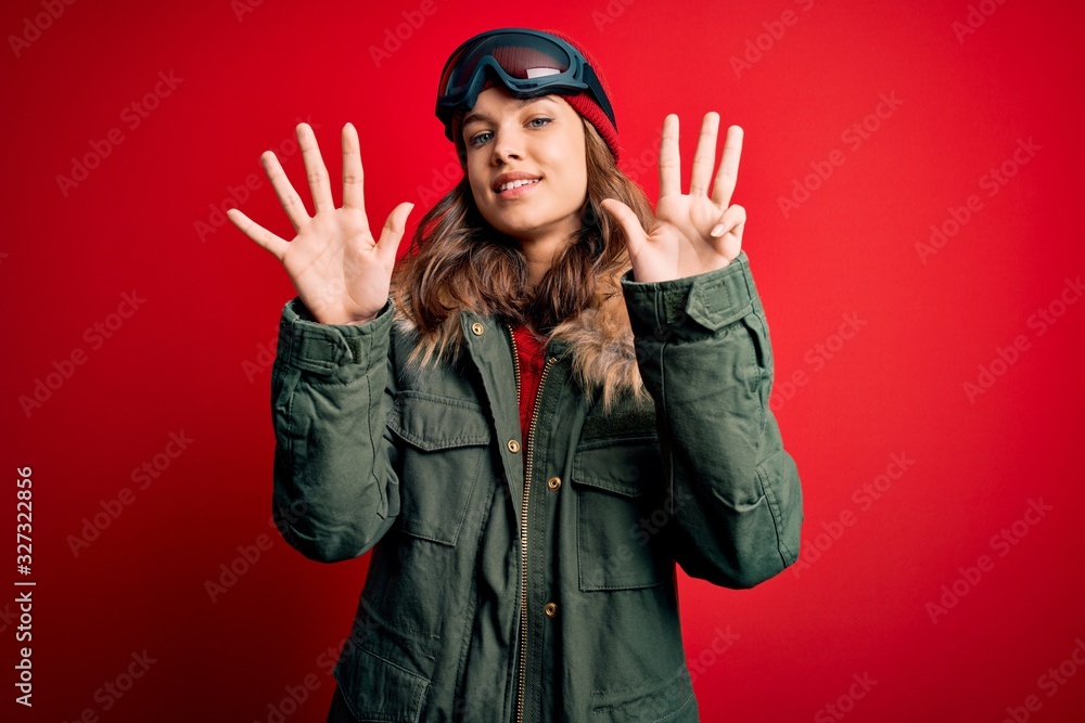 Young blonde girl wearing ski glasses and winter coat for ski weather over red background showing and pointing up with fingers number nine while smiling confident and happy. Young blonde girl wearing ski glasses and winter coat for ski weather over red background showing and pointing up with fingers number nine while smiling confident and happy.