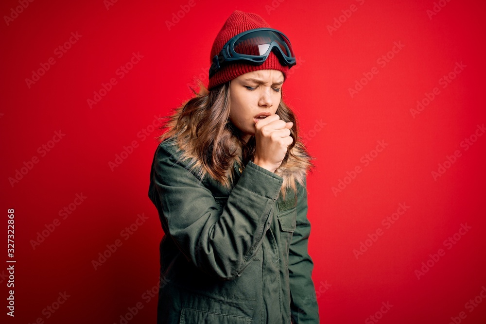 Young blonde girl wearing ski glasses and winter coat for ski weather over red background feeling unwell and coughing as symptom for cold or bronchitis. Health care concept.