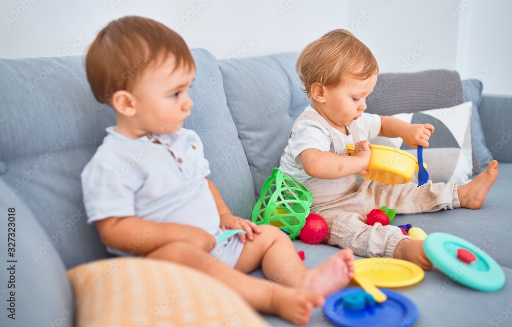 Beautiful toddlers sitting on the sofa playing with toys at home Beautiful toddlers sitting on the sofa playing with toys at home