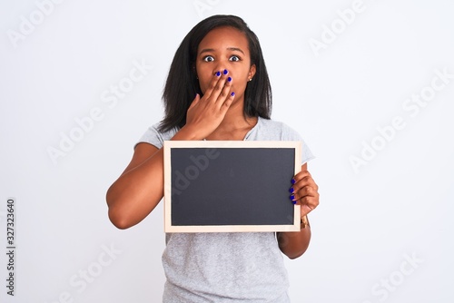 Young african american woman holding blank school blackboard over isolated background cover mouth with hand shocked with shame for mistake, expression of fear, scared in silence, secret concept