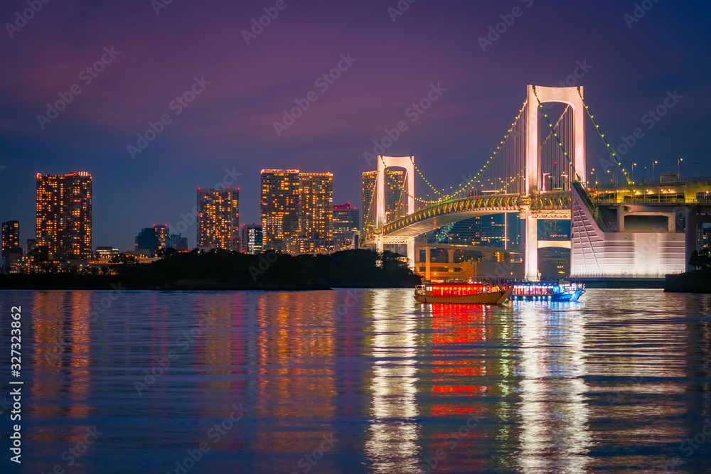 Japan. Evening in Tokyo. View of Tokyo Bay from the shore. Pleasure ships on the background of the Rainbow bridge. Panorama of the Rainbow bridge and Odaiba island. The evening lights of Tokyo.