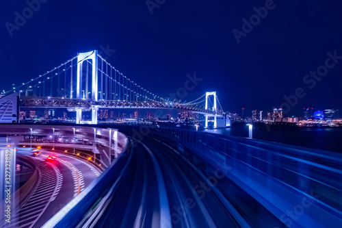 Japan. Evening panorama of Tokyo in blue. Life in the big city. Railway and road tracks on the background of the Rainbow bridge. Cars go on the highway in Tokyo. Rainbow bridge and Odaiba.