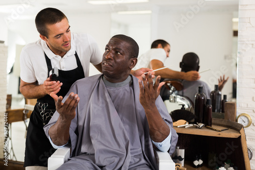 Shocked African man with confused hairdresser