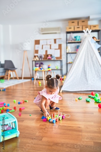 Young beautiful toddler sitting on the floor playing with wooden train toy at kindergaten photo