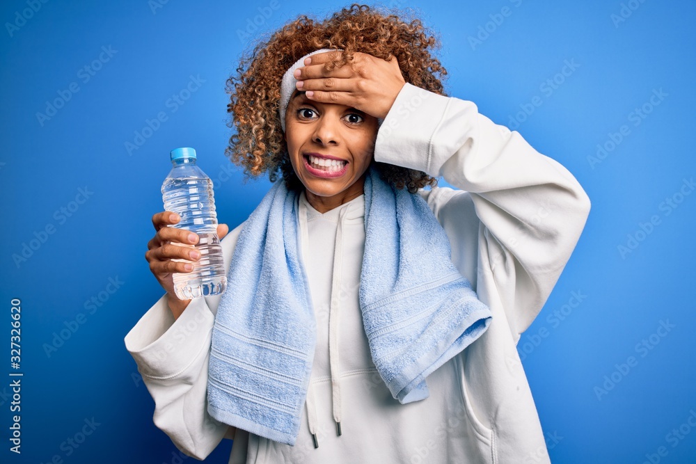 Young african american sportswoman doing sport wearing towel drinking botte of water stressed with hand on head, shocked with shame and surprise face, angry and frustrated. Fear and upset for mistake. Young african american sportswoman doing sport wearing towel drinking botte of water stressed with hand on head, shocked with shame and surprise face, angry and frustrated. Fear and upset for mistake.