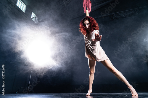Female athletic, sexy and flexible aerial circus artist with redhead dancing in the air on the silk