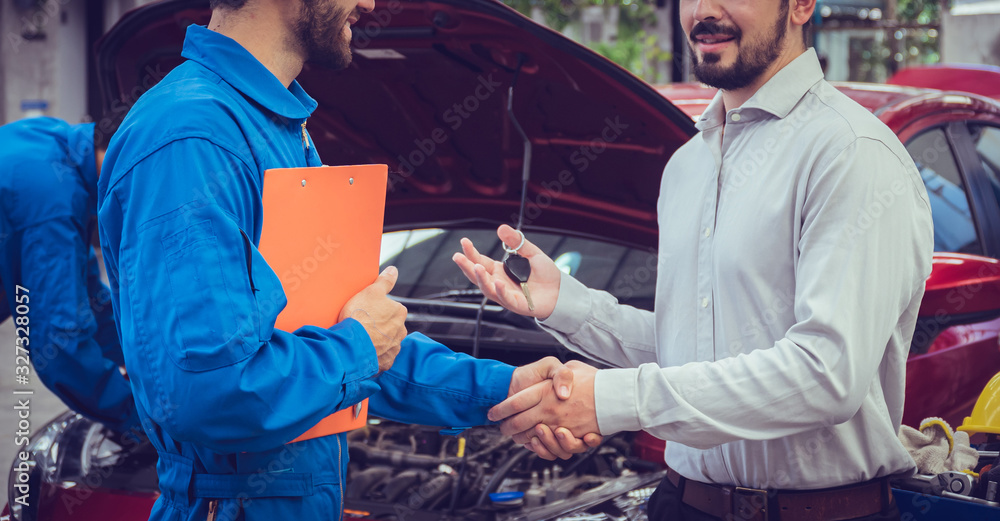 Mechanic holding clipboard shaking hands with car owner in the workshop garage. Car auto services concepts