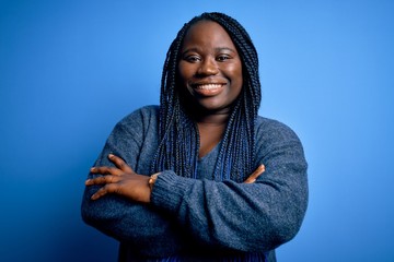 African american plus size woman with braids wearing casual sweater over blue background happy face smiling with crossed arms looking at the camera. Positive person.