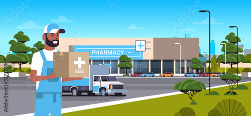 deliveryman carrying medical products in cardboard box with cross sign modern drugstore front view pharmacy store building exterior medicine healthcare delivery service concept horizontal portrait