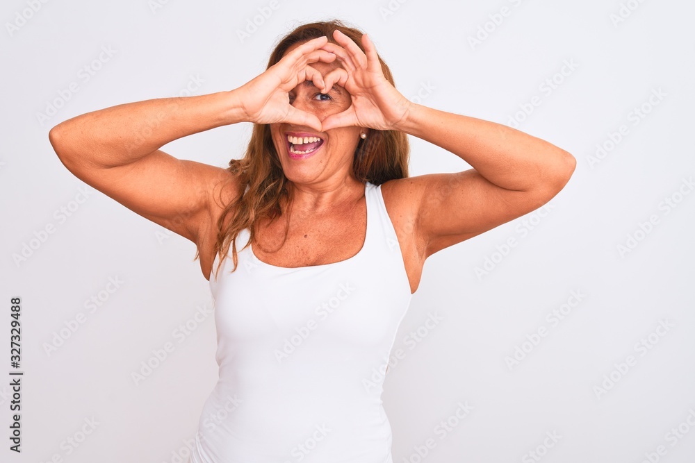 Middle age mature woman standing over white isolated background Doing heart shape with hand and fingers smiling looking through sign