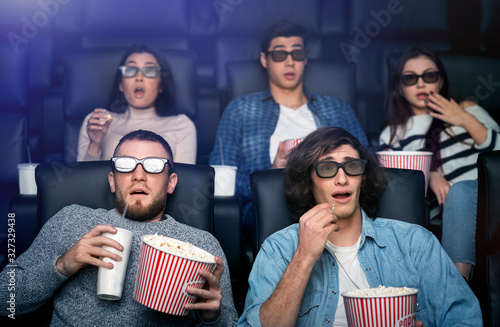 Scared people in 3D glasses watching horror movie in cinema