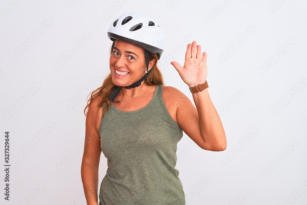 Middle age mature cyclist woman wearing safety helmet over isolated background Waiving saying hello happy and smiling, friendly welcome gesture Middle age mature cyclist woman wearing safety helmet over isolated background Waiving saying hello happy and smiling, friendly welcome gesture