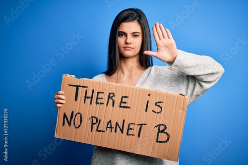 Young beautiful brunette activist woman holding banner protesting to care the planet with open hand doing stop sign with serious and confident expression, defense gesture © Krakenimages.com