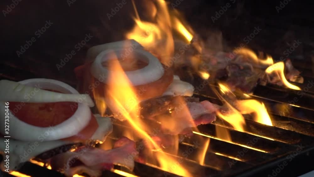 Two juicy delicious-looking burgers roast on the grill. The fire is sizzling, the flames are coming out Two juicy delicious-looking burgers roast on the grill. The fire is sizzling, the flames are coming out
