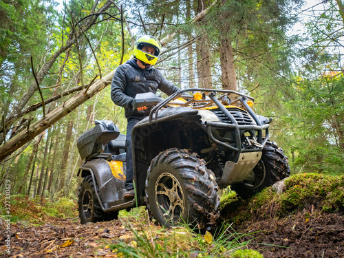 A man in a yellow helmet rides ATV the woods. Off-road Quad bike rides. Extreme entertainment. A man rides through the woods on an all-terrain vehicle. Quad bike in the forest.