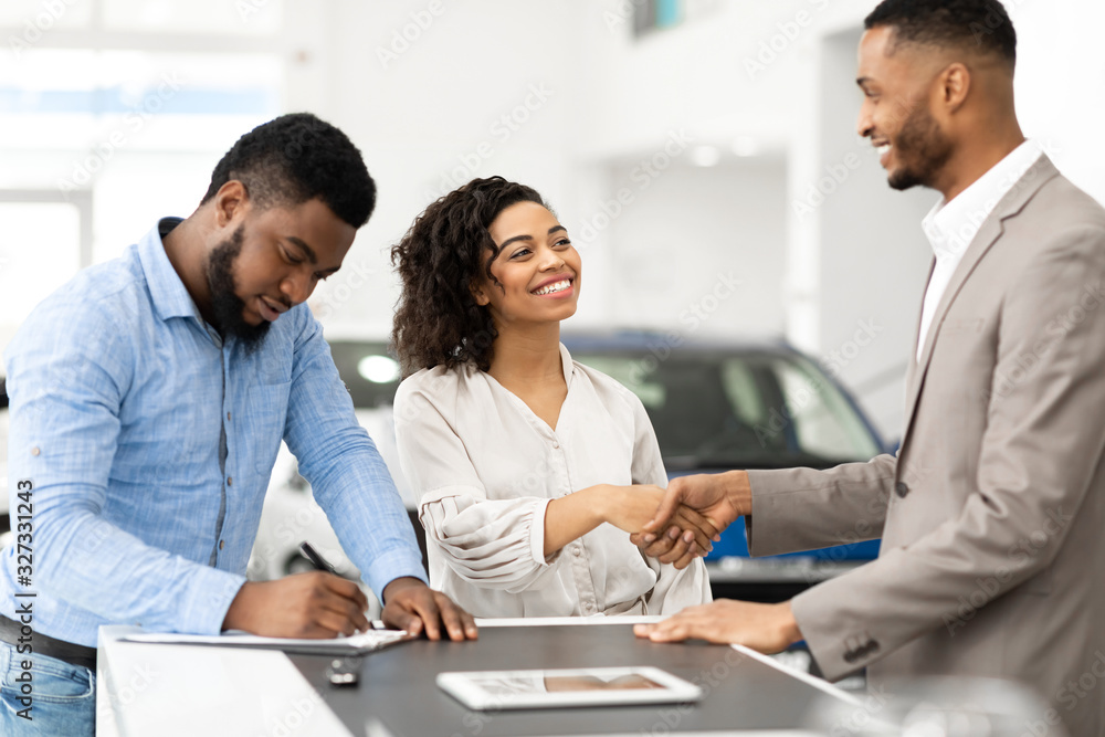 Couple Shaking Hands With Salesman In Cars Selling Center
