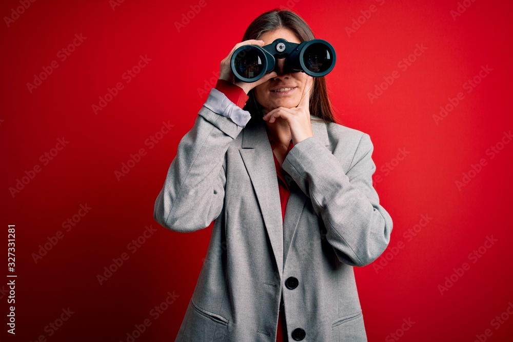 Young beautiful woman with blue eyes using binoculars over isolated red background serious face thinking about question, very confused idea Young beautiful woman with blue eyes using binoculars over isolated red background serious face thinking about question, very confused idea