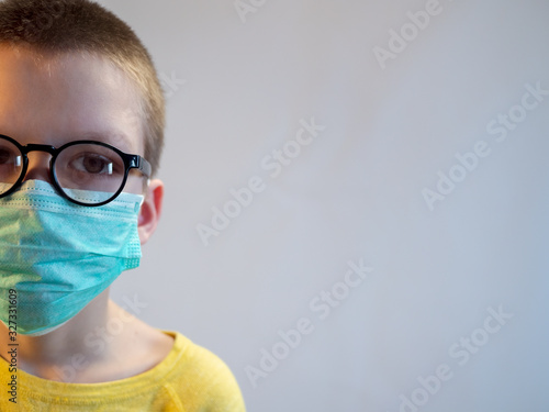 cute blonde boy in blue medical mask and glasses is quarantined at home. child coughs heavily and wears mask. concept of fight against the coronavirus epidemic and proper prevention of infections