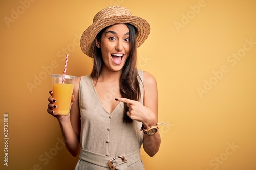 Fotografia Young beautiful woman on vacation wearing summer hat drinking healthy orange jui
