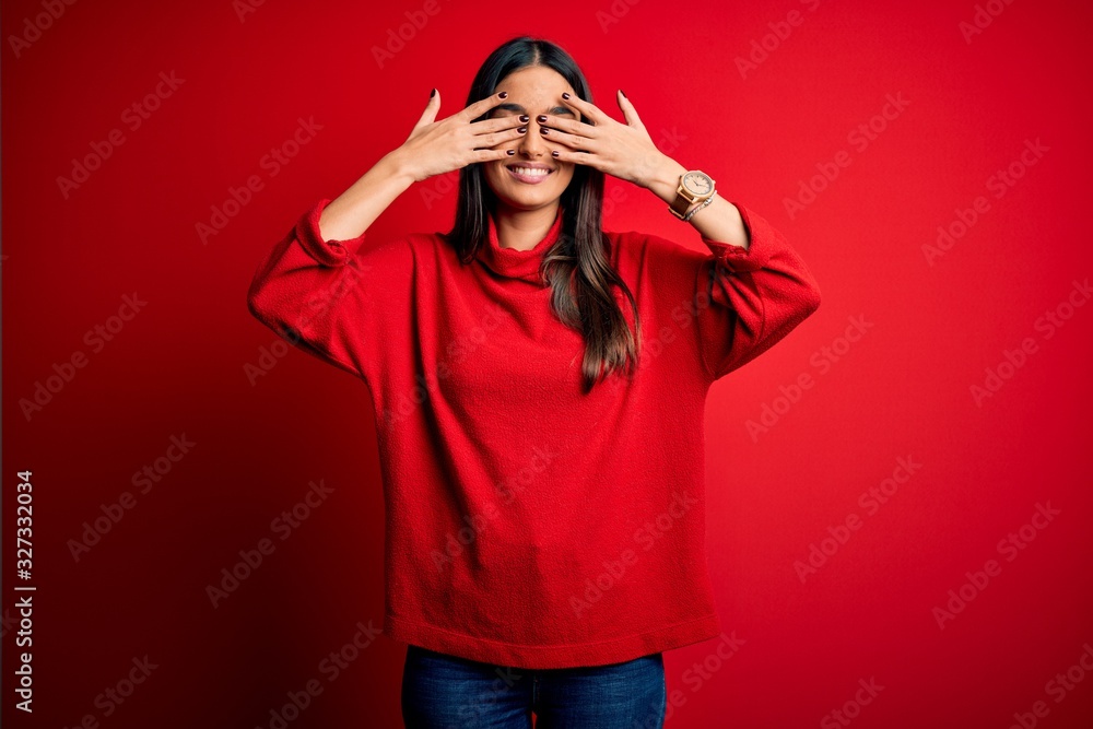 Young beautiful brunette woman wearing casual sweater over isolated red background covering eyes with hands smiling cheerful and funny. Blind concept.