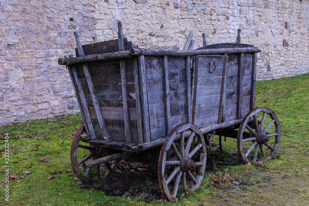 The broken ancient medieval rural wood cart or wagon on the green grass on the background of the castle or fortress stone or brick wall 