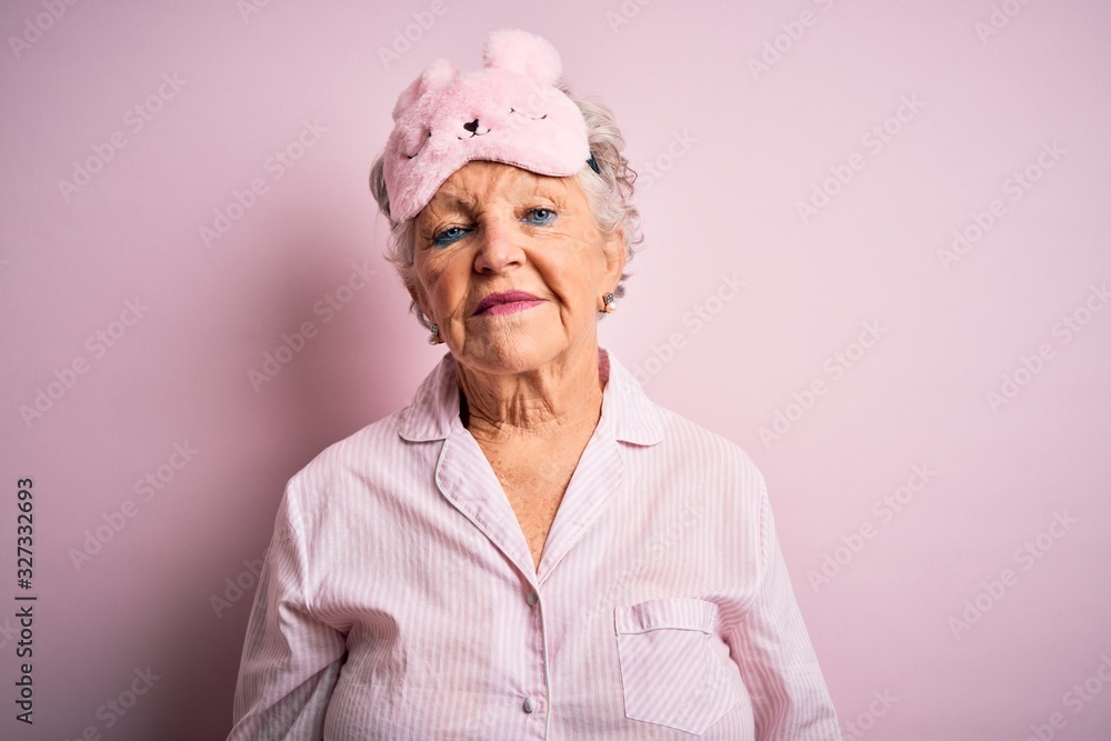 Senior beautiful woman wearing sleep mask and pajama over isolated pink background Relaxed with serious expression on face. Simple and natural looking at the camera. Senior beautiful woman wearing sleep mask and pajama over isolated pink background Relaxed with serious expression on face. Simple and natural looking at the camera.