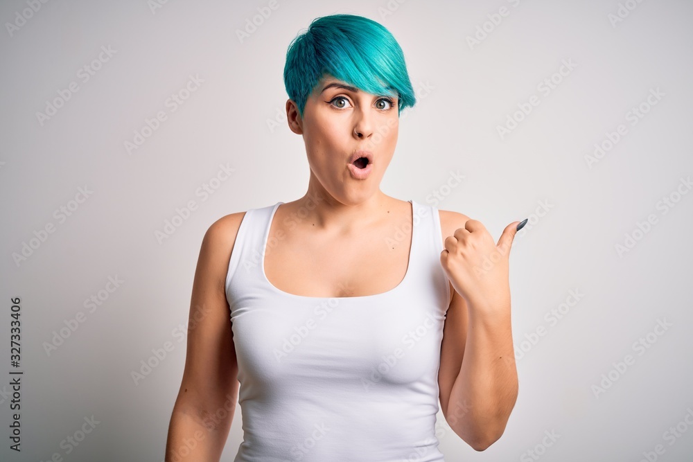 Young beautiful woman with blue fashion hair wearing casual t-shirt over white background Surprised pointing with hand finger to the side, open mouth amazed expression. Young beautiful woman with blue fashion hair wearing casual t-shirt over white background Surprised pointing with hand finger to the side, open mouth amazed expression.