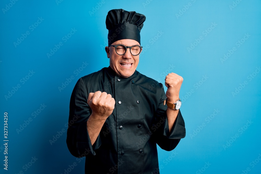 Middle age handsome grey-haired chef man wearing cooker uniform and hat celebrating surprised and amazed for success with arms raised and eyes closed. Winner concept. Middle age handsome grey-haired chef man wearing cooker uniform and hat celebrating surprised and amazed for success with arms raised and eyes closed. Winner concept.