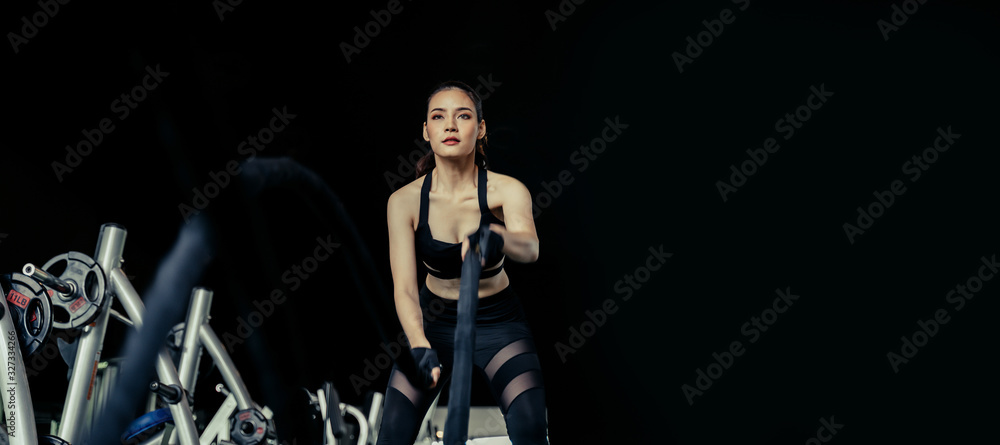 wide banner with copy space of athletic asian strong woman slim body training and working out with battle rope at fitness gym in dark background, bodybuilder, exercise fitness, workout, sport concept wide banner with copy space of athletic asian strong woman slim body training and working out with battle rope at fitness gym in dark background, bodybuilder, exercise fitness, workout, sport concept