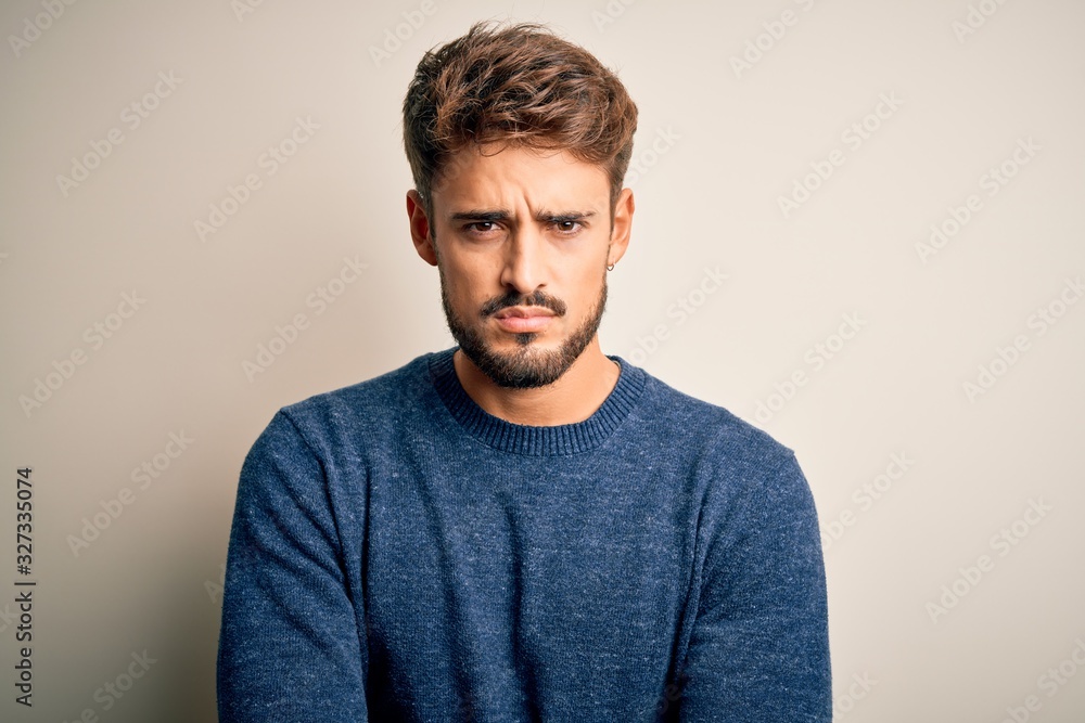 Young handsome man with beard wearing casual sweater standing over white background skeptic and nervous, disapproving expression on face with crossed arms. Negative person. - obrazy, fototapety, plakaty 