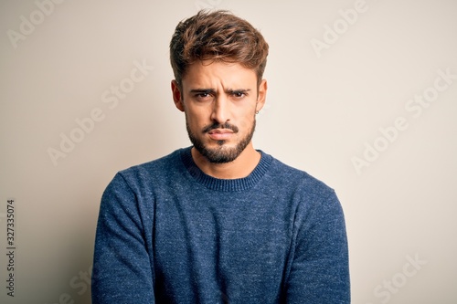 Young handsome man with beard wearing casual sweater standing over white background skeptic and nervous, disapproving expression on face with crossed arms. Negative person.