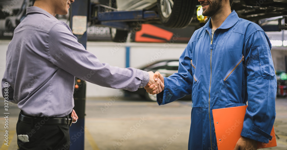 Mechanic holding clipboard shaking hands with car owner in the workshop garage. Car auto services concepts