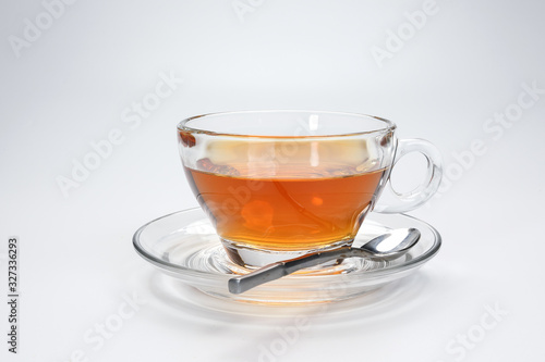 Clear licker tea in a transparent glass cup saucer spoon on white background
