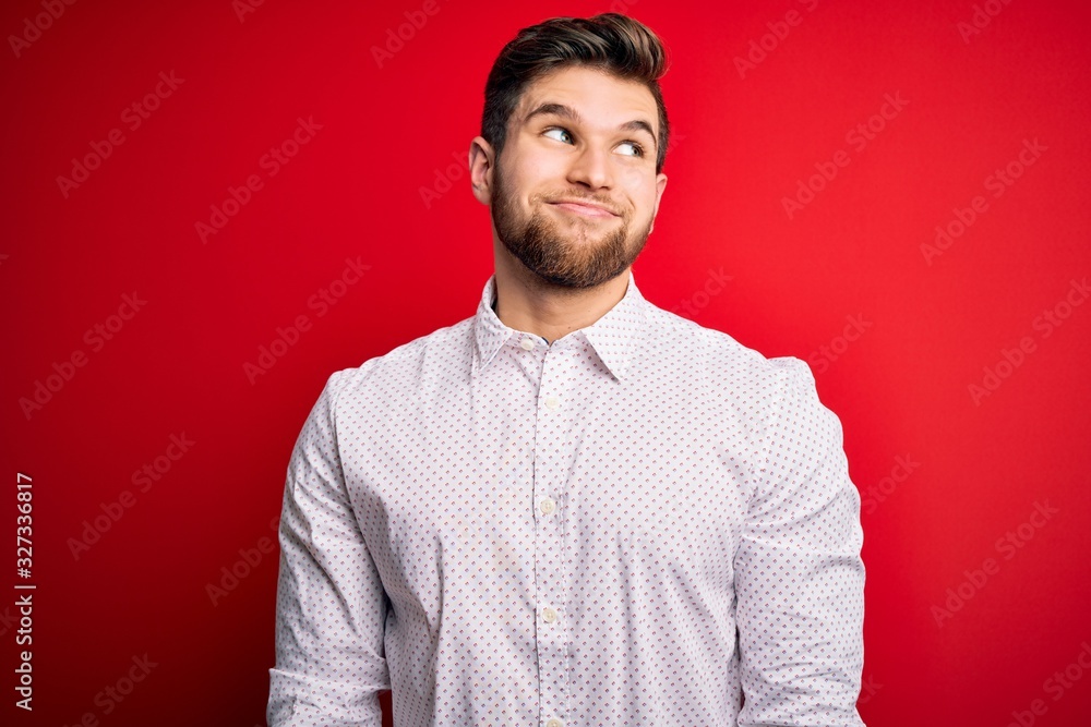 Young blond businessman with beard and blue eyes wearing elegant shirt over red background smiling looking to the side and staring away thinking. Young blond businessman with beard and blue eyes wearing elegant shirt over red background smiling looking to the side and staring away thinking.