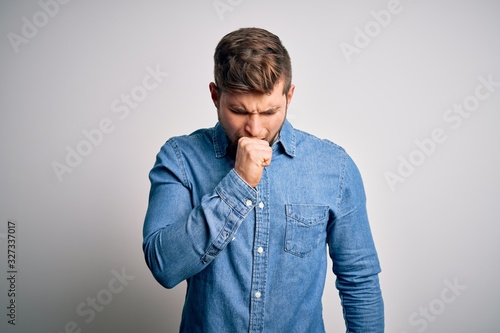 Young handsome blond man with beard and blue eyes wearing casual denim shirt feeling unwell and coughing as symptom for cold or bronchitis. Health care concept.