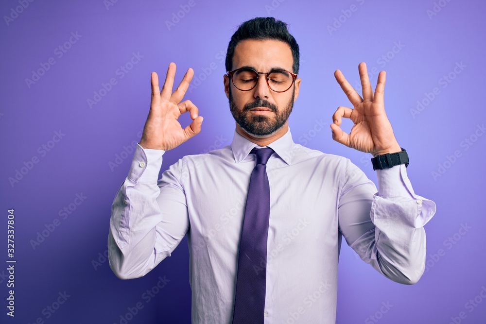 Handsome businessman with beard wearing casual tie and glasses over purple background relax and smiling with eyes closed doing meditation gesture with fingers. Yoga concept. Handsome businessman with beard wearing casual tie and glasses over purple background relax and smiling with eyes closed doing meditation gesture with fingers. Yoga concept.