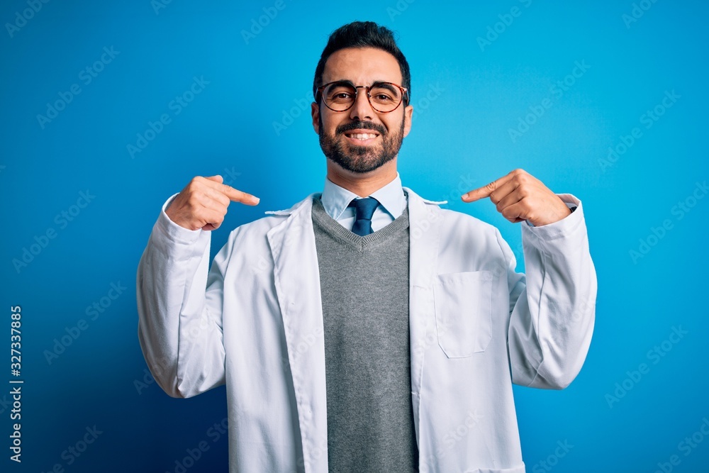 Young handsome doctor man with beard wearing coat and glasses over blue background looking confident with smile on face, pointing oneself with fingers proud and happy. Young handsome doctor man with beard wearing coat and glasses over blue background looking confident with smile on face, pointing oneself with fingers proud and happy.