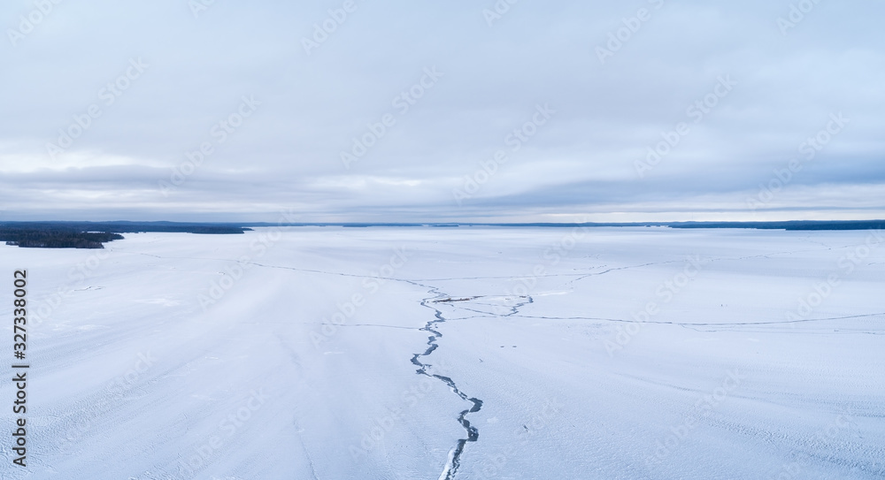 Beautiful huge lake in Finland at cloudy day.  Lake surface with big cracks. Aerial photography during winter season.