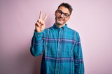 Young handsome man wearing casual shirt and glasses standing over isolated pink background showing and pointing up with fingers number two while smiling confident and happy.