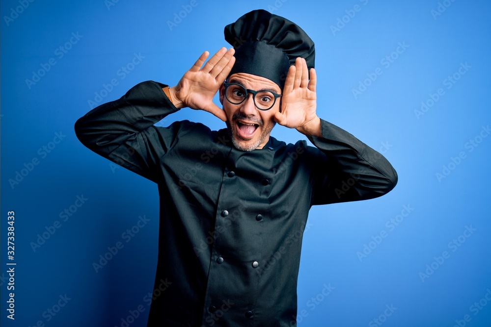 Young handsome chef man wearing cooker uniform and hat over isolated blue background Smiling cheerful playing peek a boo with hands showing face. Surprised and exited Young handsome chef man wearing cooker uniform and hat over isolated blue background Smiling cheerful playing peek a boo with hands showing face. Surprised and exited