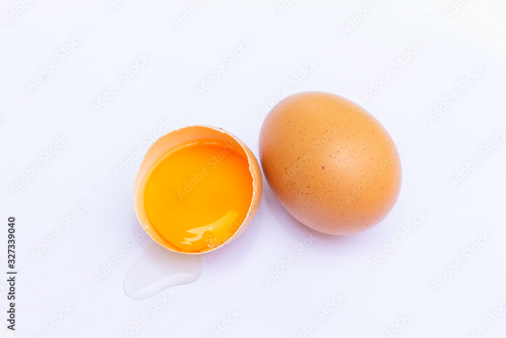 Two brown eggs With one egg broken in half, with a yolk inside the eggshell, laid on a white background