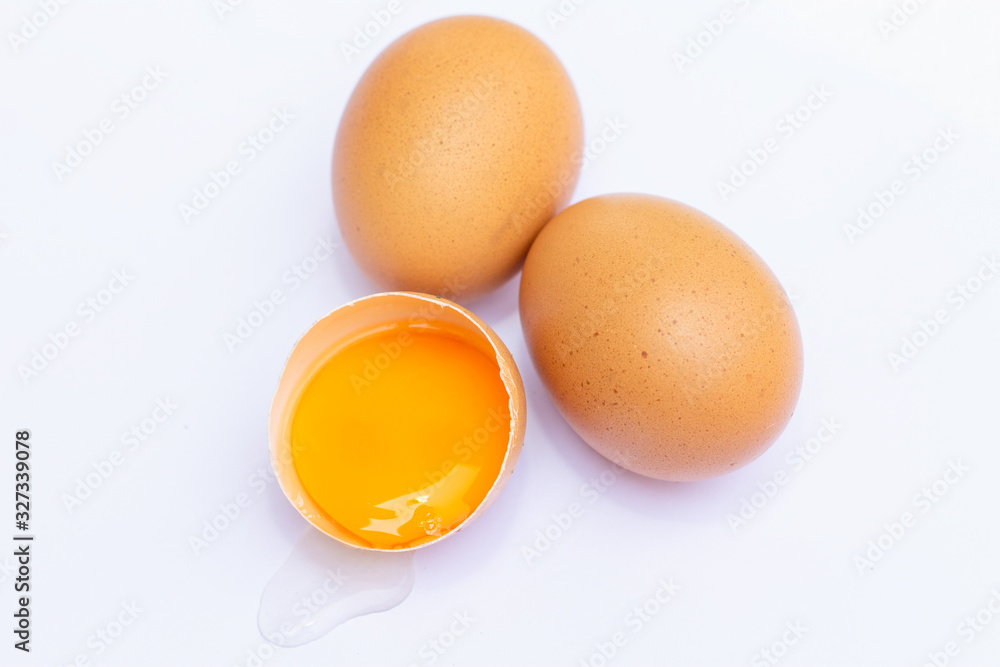Three brown eggs With one egg broken in half, with a yolk inside the eggshell, laid on a white background Three brown eggs With one egg broken in half, with a yolk inside the eggshell, laid on a white background