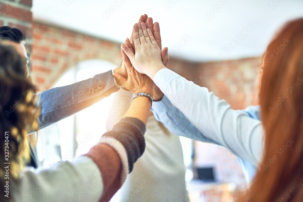 Group of business workers standing with hands together highing five at the office - obrazy, fototapety, plakaty 