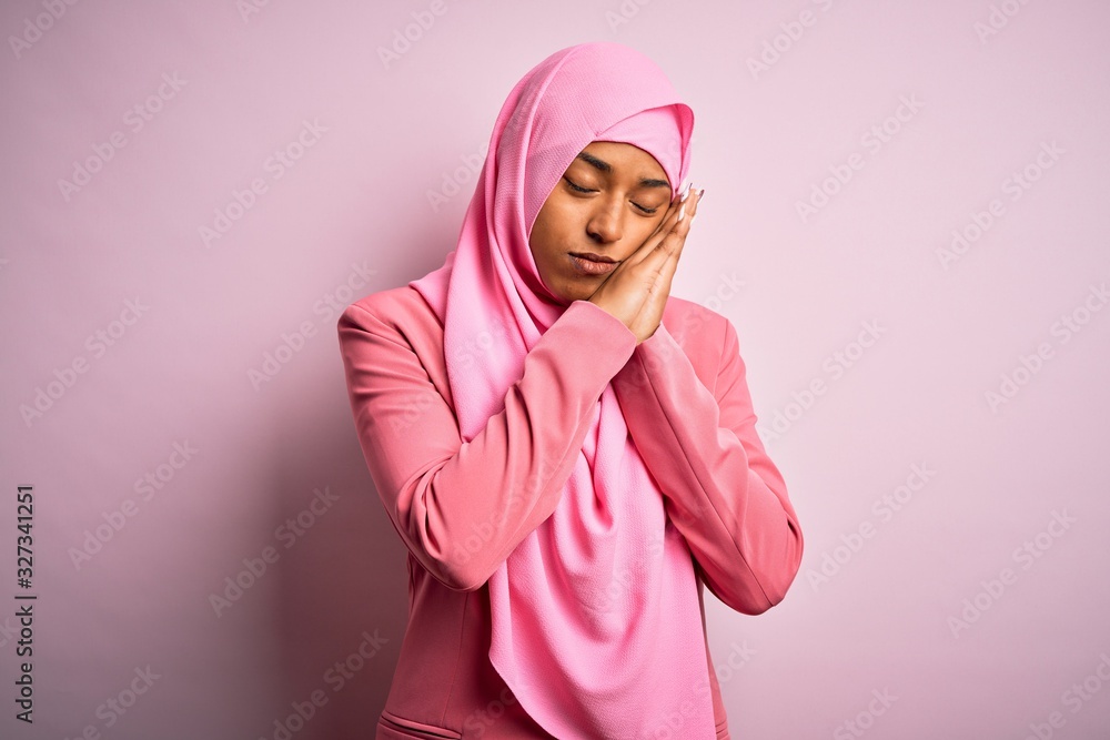 Fototapeta premium Young African American afro woman wearing muslim hijab over isolated pink background sleeping tired dreaming and posing with hands together while smiling with closed eyes.