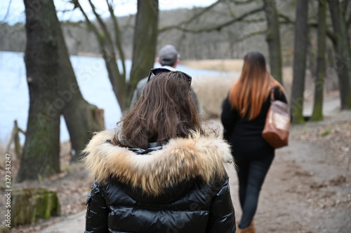 An young couple is hiking at a lake in Berlin-Germany on a cold winter day while a young woman follows them.