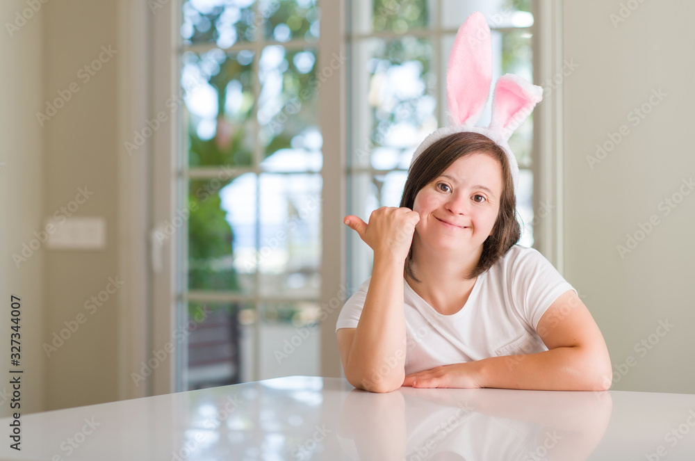 Down syndrome woman at home wearing easter rabbit ears pointing and showing with thumb up to the side with happy face smiling Down syndrome woman at home wearing easter rabbit ears pointing and showing with thumb up to the side with happy face smiling
